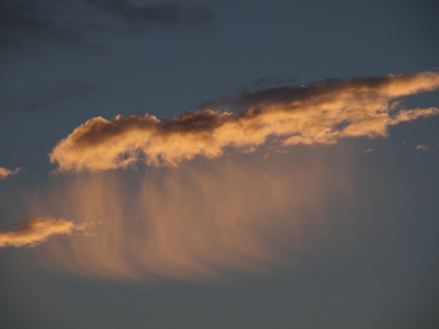 [A close view of a cloud with wisps of white below most of it. The top part of the cloud is a very dark color while the rest is creamy white against the blue sky.]